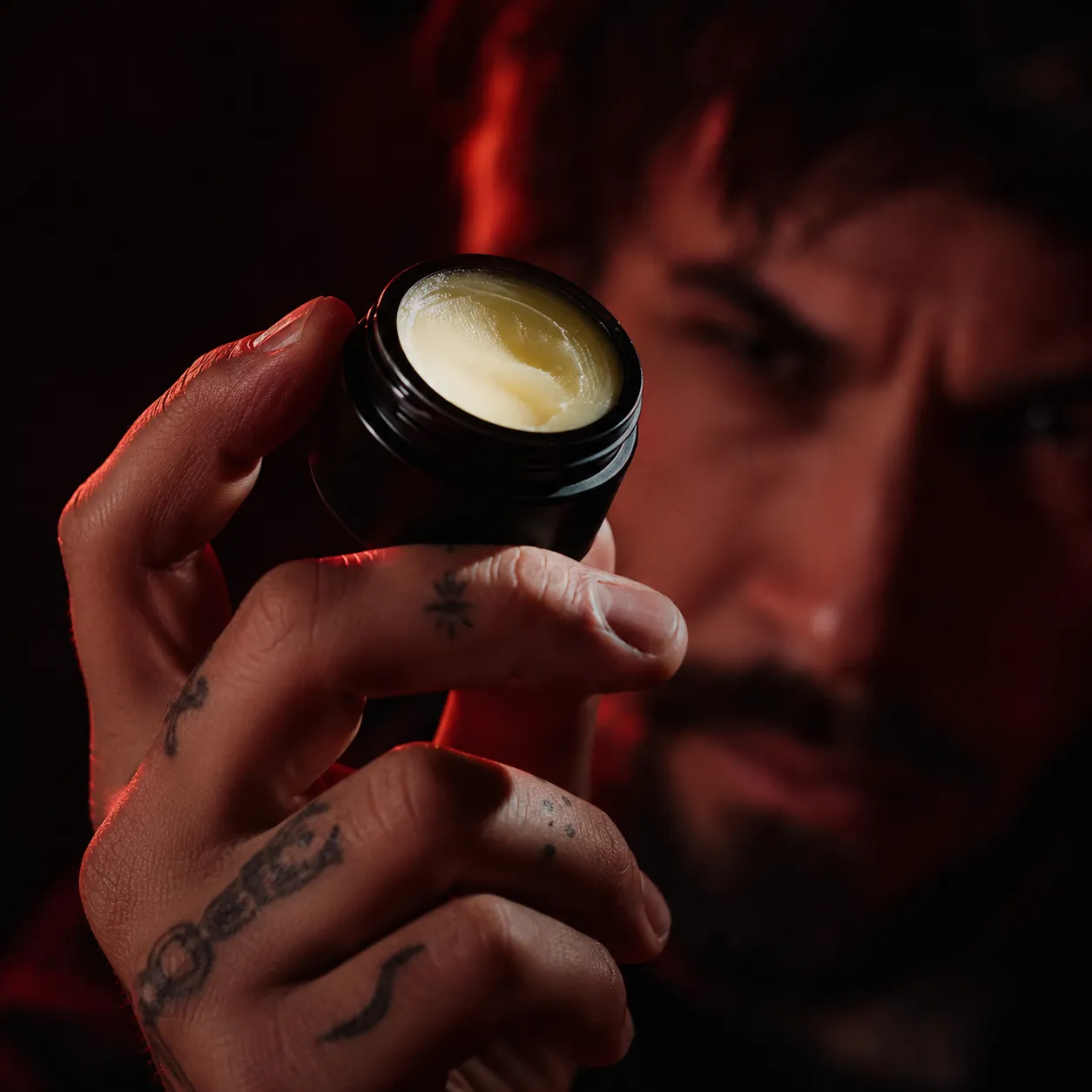 A person holding an open jar of cannabis topical cream