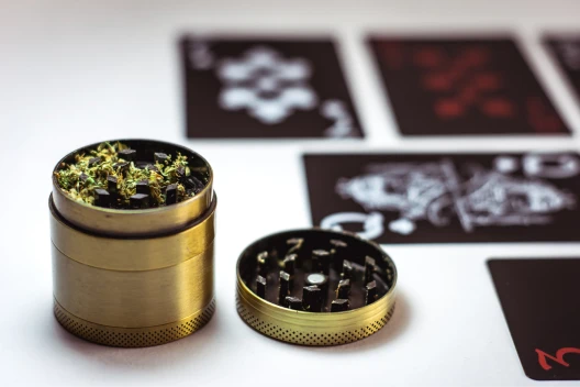 A grinder with cannabis buds sits in front of a set of cards