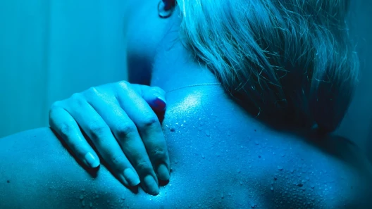Cannabis user under blue light rubbing topical cream on their shoulder